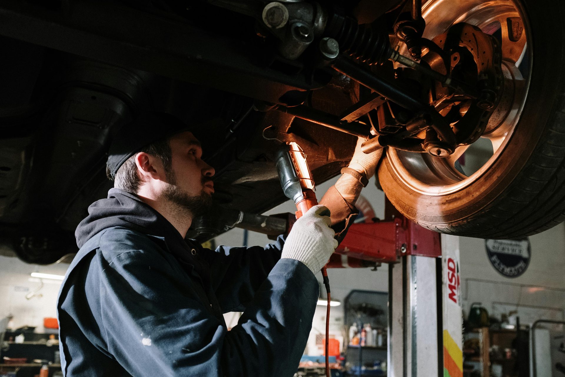 Mecánico examinando los bajos de un coche en un taller, centrándose en el mantenimiento del vehículo.